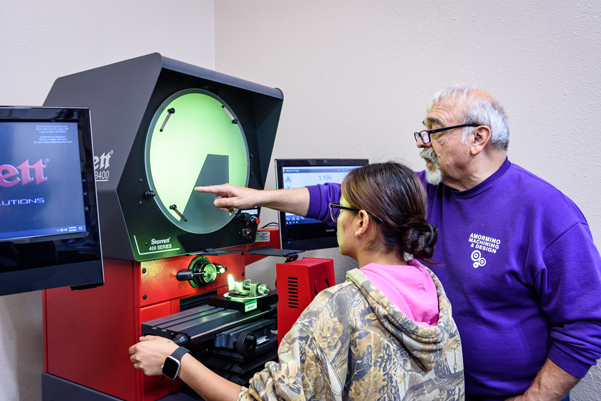 A student and instructor confer over the student's use of specialized equipment. The teachers points to something on the screen that the student needs to make note of.